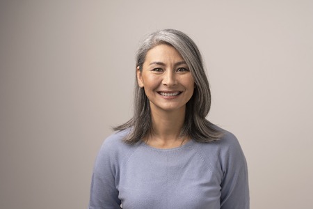 Charming Middle-Aged Asian Woman Broadly Smiles At Camera. Horizontal Studio Shot Of Graceful Smiling Woman. Portrait