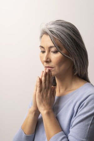 Pensive Mongolian Female Appearance on a White Background. The Look of the Woman is Sadly Lowered. She Thought Folding Her Arms in Front of Her Faces. Close Up Shoot.の写真素材