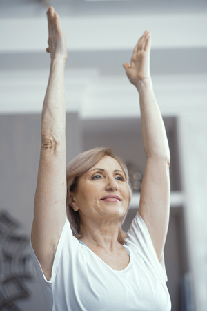 A Woman Over 50 Years Old Loves Yoga. She Raised Her Hands in the Pose of Asana. She Likes Yoga at Home. Close Up Shot.の写真素材
