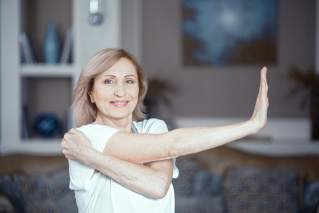 Pleasant Middle Aged Woman With Blond Hair Stretching Left Hand. Doing Yoga At Home. Health Concept.の写真素材
