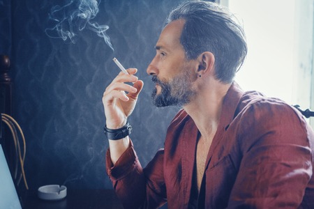 Close Up Profile of a Man With a Beard. The Appearance of a Man Tooks Brutal. Stylish Man Smoking a Cigarette With a Serious Face.の写真素材