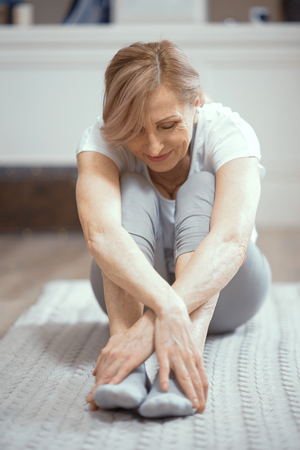 Healthy Mature Woman Relaxing After Yoga Exercises. Crossed Hands On Legs. Sitting On Yoga Mat. Yoga Practice Concept.の写真素材