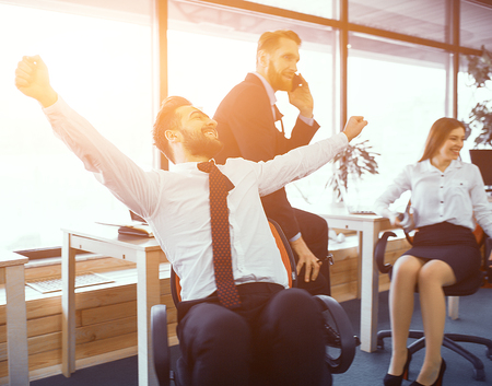 Man With Hands Up Having Fun In Sunny Modern Office. Sitting On Chair. Relaxed Working Environment After Meetingの写真素材