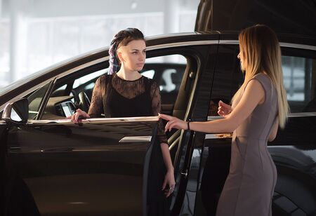 Girl is Testing New Electric Car in Auto Show Indoor. Beautiful Girl with Blue Dreads is Talking to Automobile Advisor in Car Showroom and Going to Make big Purchase. Luxury Premium Class Vehicle. Kyiv, Ukraine, F-Drive showroom 13 of february 2018.のeditorial素材