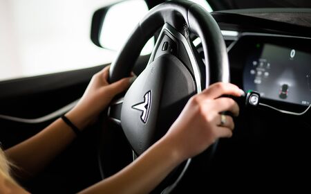 Steering Wheel of Luxury Tesla Vehicle. Female is Driving New Generaton Electro-Hybrid Automobile by...