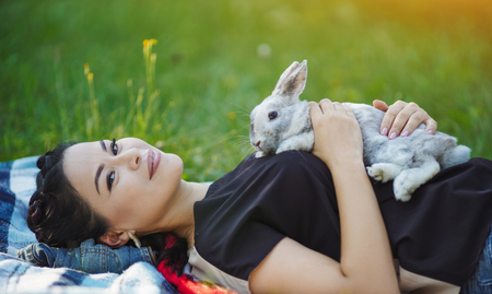 Young Asian Hugging Rabbit on Green Grass. Lovely Summer Picnic. Girl Laying on Grass.の写真素材