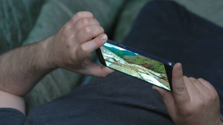 Man lying on couch and watching video about nature in high definition through Huawei Mate 20 X...