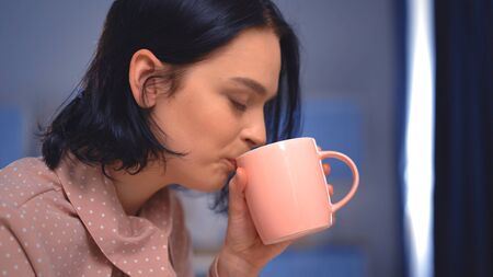 The Good-looking Young Woman Is Drinking A Beverage With Closed Eyes.She Is Wearing An Elegant Pink...
