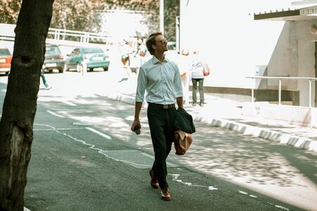 The Well-Dressed Man Is Having A Walk Around The City. He Is Holding A Jacket And A Brown Briefcase In One Hand And A Coffee Cup In The Other. He Is Looking Aside With Interest. Toned image.の写真素材