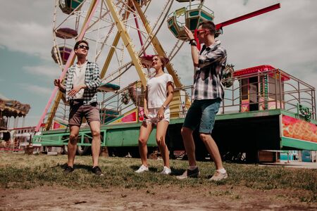 Friends Hanging Out In The Theme Park.Two Boys And A Girl Are Dancing.A Ferris Wheel Are On The...