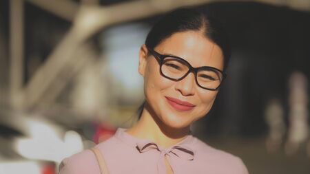 Asian middle-aged woman happily smilling in sun rays. A brunet businesswoman in glasses laughing. Portrait on a blured back.の写真素材