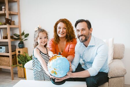 Smiling parents and daughter holding globe, planning vacation. Family travel concept, mom, dad and little girl choosing where to go.の写真素材