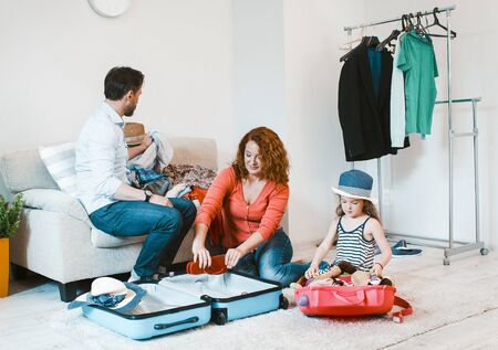 Happy family going on vacation. Mom, dad nad little daughter packing suitcase.の写真素材