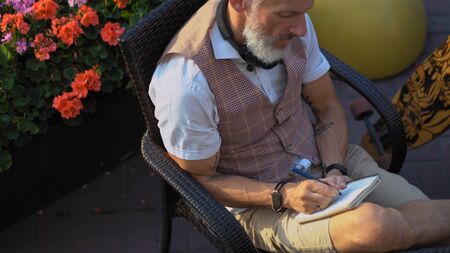 The traveling author in the asual makes notes in a notebook on a summer day during a longboard ride break. Shoted from above.の写真素材