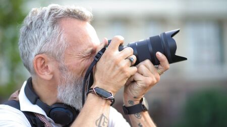 A Beautiful Caucasian Man With A Camera In His Hands Makes A Professional Shot. Profile View. Close Up.の写真素材