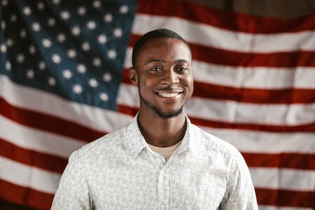 Charming Black Guy Dressed In White Shirt Cheerful Smiles Patriotically Posing On American Flag...