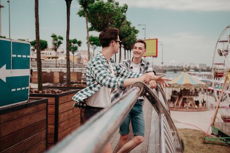 Students On Vacation. Two European Guys In Plaid Shirts Cheerfully Talk Together In The Background Of The Amusement Park.の写真素材