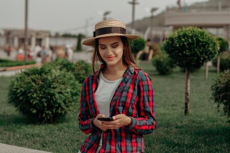 The Girl Received A Message From Her Friend. A European Brunette In A Straw Hat Smiles Reading A...