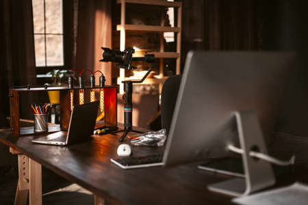 A Mirrorless Digital Camera On Gimbal Stabiliser, Unique Table Lamp, Computer, Laptop Are On A...
