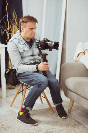 Funny Photographer In Casual Holding Mirrorless Digital Camera On Gimbal Stabiliser, Serious Creative Man Professional Male Reporter Looking Thoughtfully Choosing The Best Focus For The Photo..の写真素材