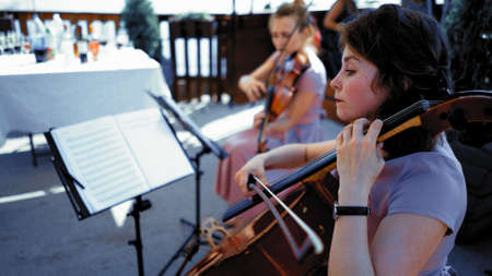 Intelligent female musician plays the cello outdoor. Caucasian woman holds a bow in one hand and clamps the strings of cello with the other, Woman Violinist plays the violin on blurred backgroundの写真素材
