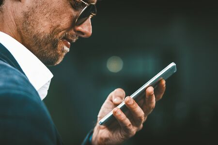 Handsome businessman answering text messsges or serching information online. Man in business sute and sunglasses with telephone or smartphone in his hand.の写真素材