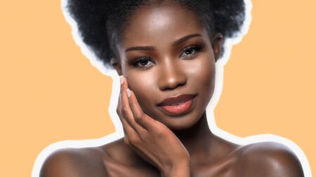 Attractive African Woman With Bare Shoulders Isolated On Cream Color Background, Portrait Of Dark-Skinned Woman With Clean Healthy Skin Touches Face With Hand, Skin Care Conceptの写真素材