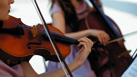 Musical Orchestra Of Female Musicians Plays On The Summer Terrace Outside, Hands Holding A Violin And Bow, Close Upの写真素材