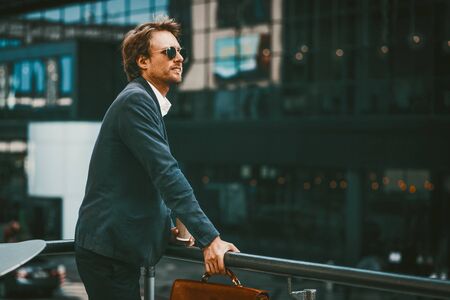 Handsome brown-haired businessman in blue sute standing outside of business center and having catch of a fresh airの写真素材
