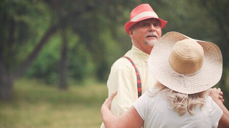 Elegant Grandfather Is Dancing With His Beloved Grandmother In The Garden. The Woman Is Standing With His Back. The Concept Of Happy Old Age.の写真素材