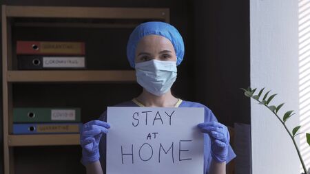Female Medic Demonstrate Slogan To Stay At Home Written With Marker On Paper, Doctor In Blue Gloves...