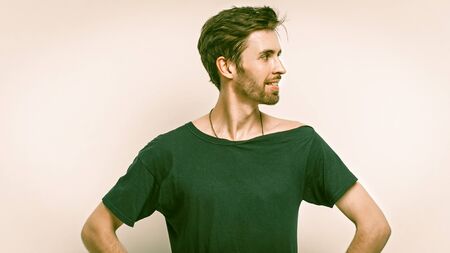 Smiling Man Stands With Arms Akimbo, Front View Portrait Of Caucasian Man In Black T-Short Looking At Right Side, Isolated On Grey Background, Studio Shot With Copy Space At Right Sideの写真素材