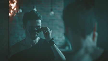 Elegance Man In Sunglasses Reflected In Blue Mirror, Caucasian Bearded Man Looking In Mirrot At Night Indoor, Rear Viewの写真素材