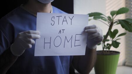 Doctor Or Nurse Shows Sign To Stay At Home, Male Medic In Blue Uniform Demonstrates Inscription On...