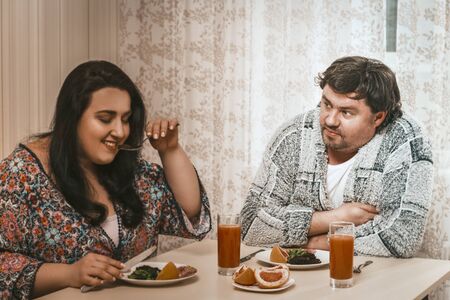 Plus Size Couple About To Eat Healthy Food, Selective Focus On Man In Casual Clothes Looking On Woman Holding Fork In Foreground And Testing Salad From Plateの写真素材