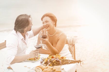 Mid aged couple with red wine sit in restaurant in beautiful style. Happy elderly concept.の写真素材