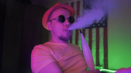 Hipster Exhales Cloud Of Smoke Smoking A Hookah, Caucasian Man Wearing Hat And Sunglasses Resting...