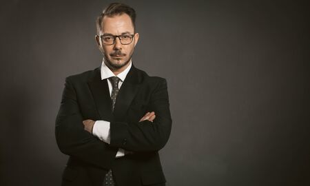 Businessman stands arms crossed on grey background. Caucasian confident man looks at the camera...