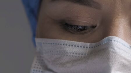 Tired doctors eye. Woman in protective mask looks down, young woman exhausted from overworking...