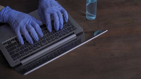 Hands in gloves typing on the laptop keyboard. Necessary preventive measure in the fight against the coronavirus. Pandemic lifestyles concept.の写真素材