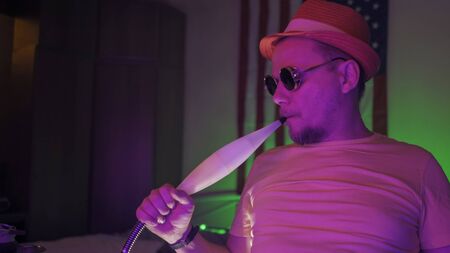 Hipster has fun self-isolation during quarantine. American man in sunglasses smokes hookah. Cheerful...