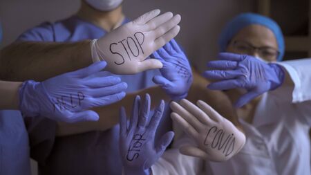 Background from the hands of doctors with open palms in multi-colored disposable gloves with the inscriptions stop covid test help on them. Pandemic concept.の写真素材
