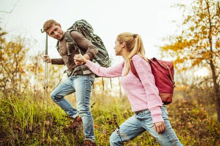 Man helps a woman climb a hill holding womans hand and hiking poles in other hand. Hiking concept....