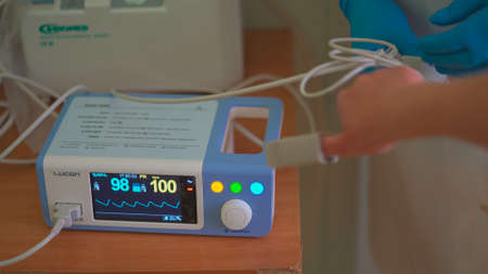 Pulse Oximeter at work. Medical diagnostic equipment. Patients hand with attached pulse oximeter sensor element in blurred foreground. City Hospital. May, 2020, Brovary, Ukraine.のeditorial素材