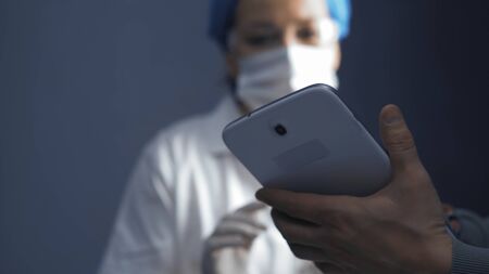Female doctor or nurse learning to use an electronic notepad gadget. Focus on electronic device in male hands in the foreground. Education concept. Close up shot. Toned image.の写真素材