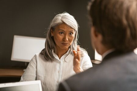 Business discussion of woman and man. Mature Asian woman expressively grimaces to be convincing in...