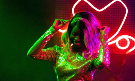 Fashionable girl dancing in night club. Cheerful African American woman dancing among the bright neon lights. Party concept. Lifestyle concept.の写真素材