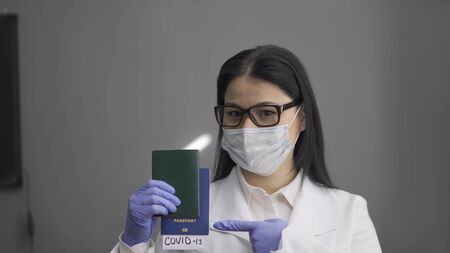Doctor holds passports with Covid 19 insert. Asian woman holding dangerous disease test results while looking at camera. Tourism concept. Coronavirus outbreak concept.の写真素材