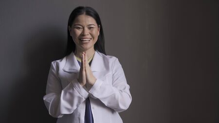 Happy doctor laughs joyfully clasped her hands together while standing against the gray wall....