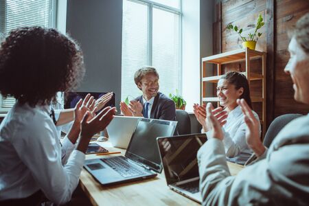 Friendly colleagues cheerfully laugh and applaud each other. Men and women clap their hands to mark ended of successful teamwork. Toned image.の写真素材